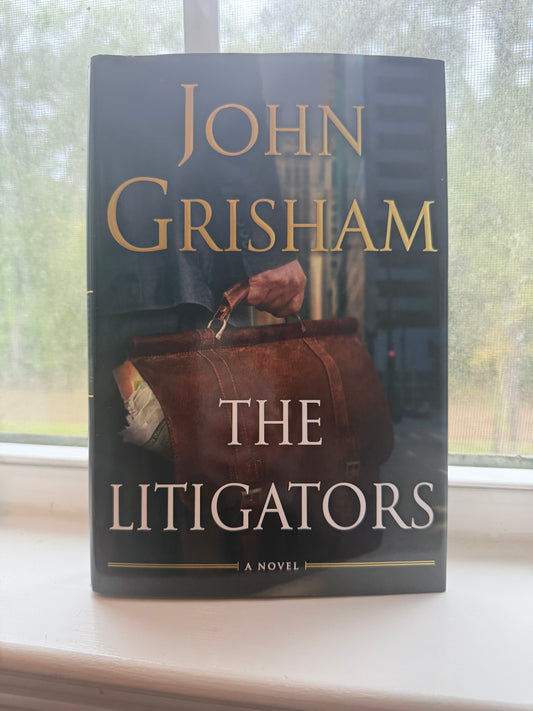 Book titled 'The Litigators' by John Grisham on a reflective surface
