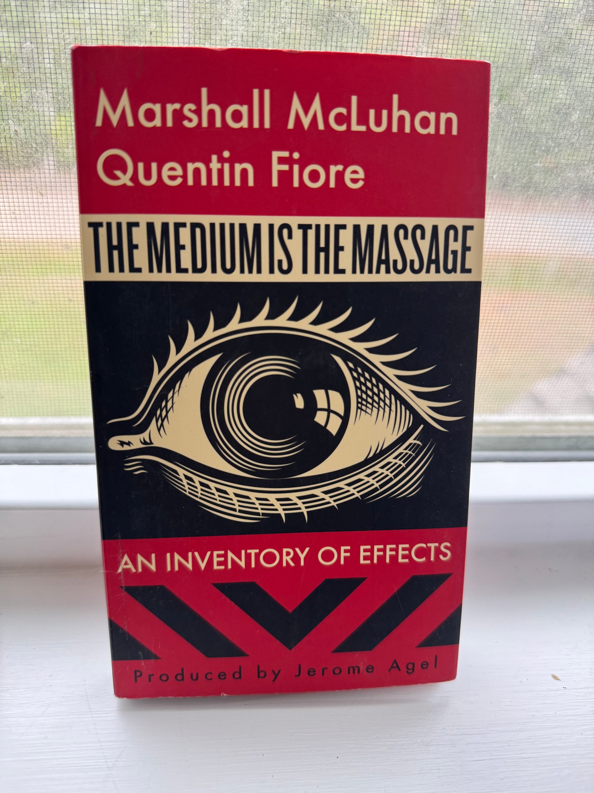 Book titled 'The Medium is the Message' by Marshall McLuhan and Quentin Fiore on a window pane.