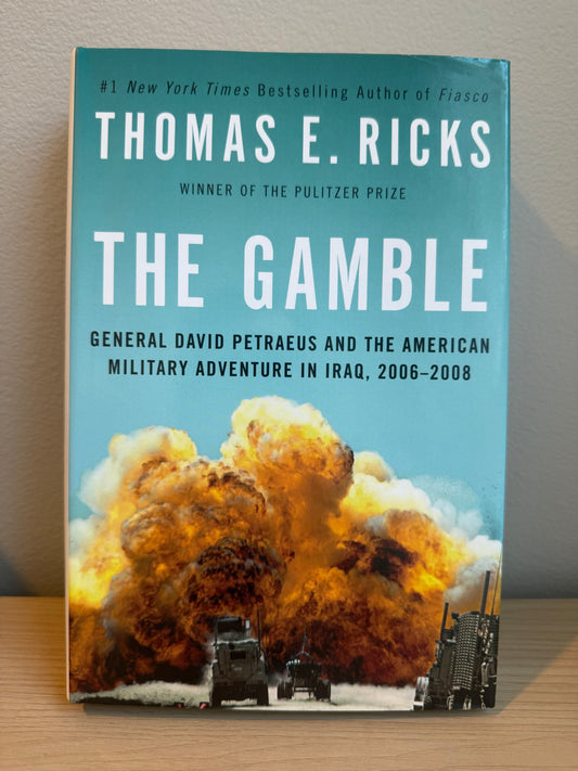 Book titled 'The Gamble' by Thomas E. Ricks with an explosion image on a wooden surface.