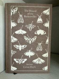 Book titled 'The Hound of the Baskervilles' with moth illustrations on a brown cover.