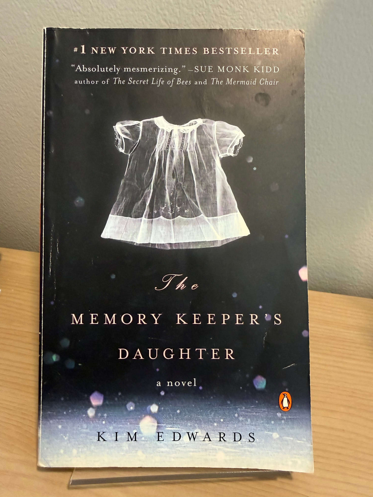 The book cover of 'The Memory Keeper's Daughter' by Kim Edwards, published by Penguin, displayed on a light-colored wooden surface.