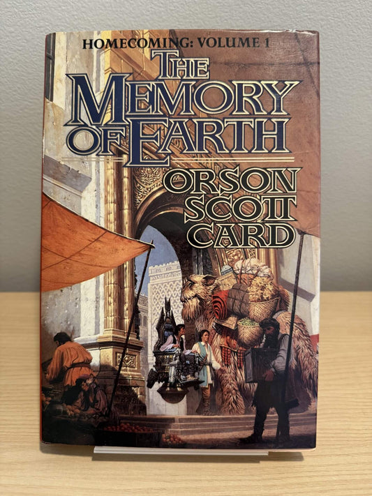Book cover of 'The Memory of Earth' by Orson Scott Card on a wooden surface with a neutral background