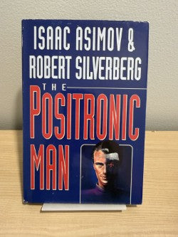 Book cover of The Positronic Man by Asimov and Silverberg on a wooden surface.