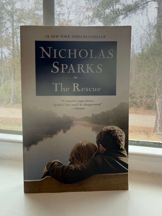 Book titled 'The Rescue' by Nicholas Sparks on a surface with a window in the background