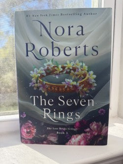 Book titled 'The Seven Rings' by Nora Roberts on a windowsill.