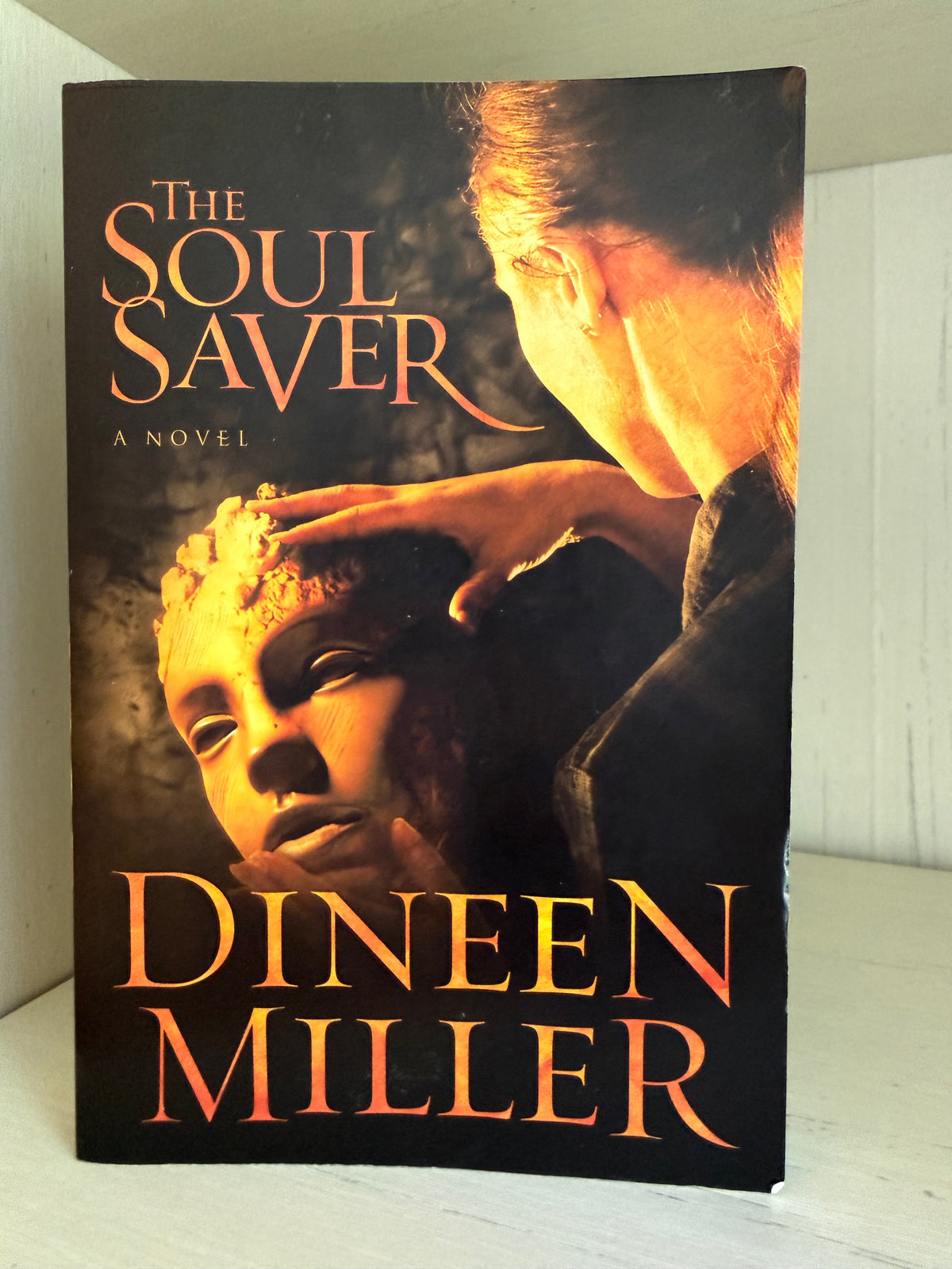 The book cover of 'The Soul Saver' by Dineen Miller, featuring a dramatic illustration of a woman touching a child's face, with the title and author name in orange lettering on a dark background.
