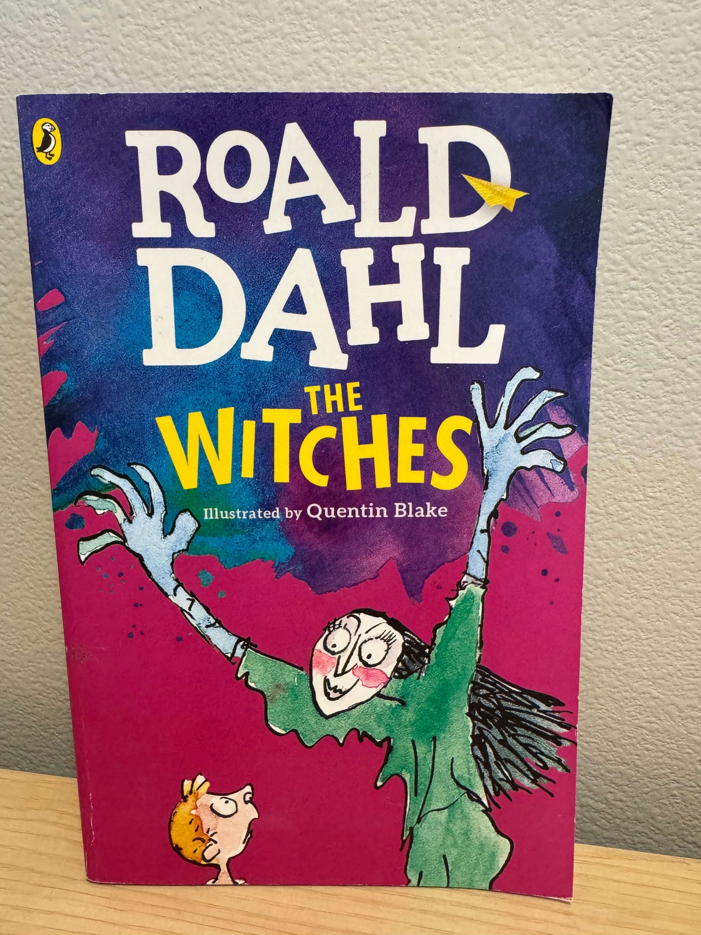 The front cover of the book 'The Witches' by Roald Dahl, illustrated by Quentin Blake, published by Penguin. The cover features a vibrant magenta-pink background with a green witch character with outstretched hands and a small blonde child at the bottom.