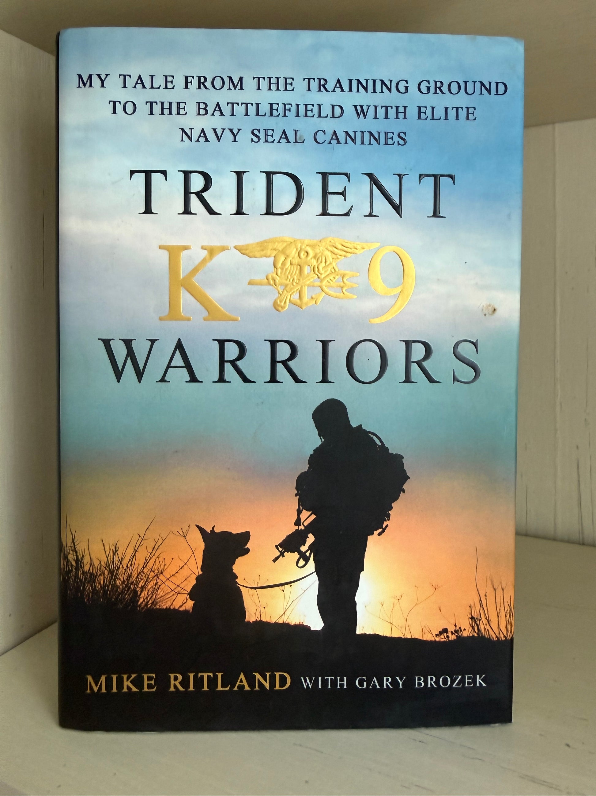 The book cover of 'Trident K-9 Warriors' by Mike Ritland with Gary Brozek, featuring a silhouette of a K-9 handler and dog against a sunset sky on the front cover.