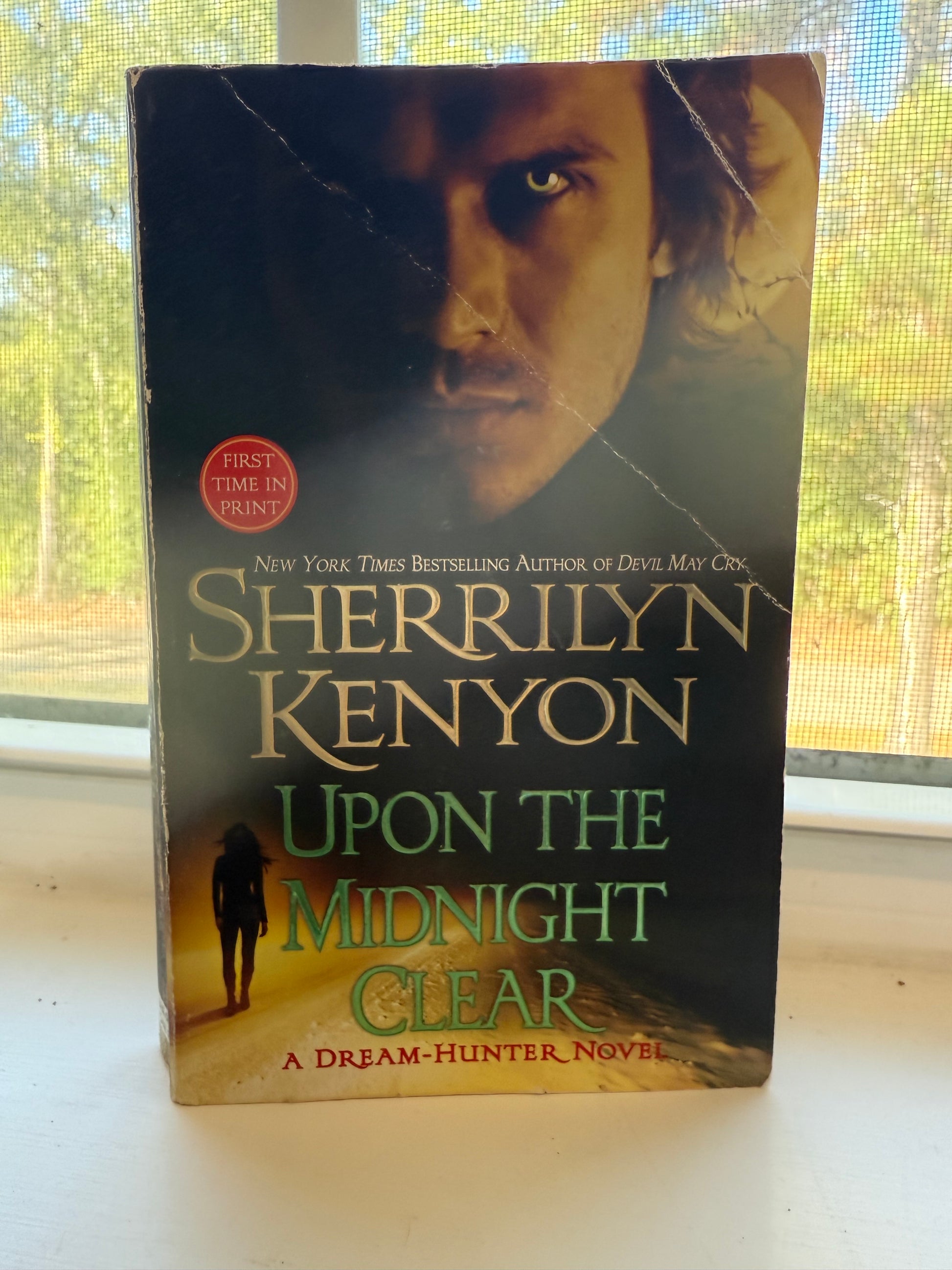 Book titled 'Upon the Midnight Clear' by Sherrilyn Kenyon on a surface with a window in the background.