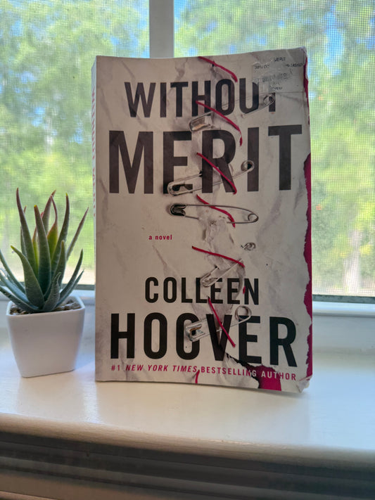 Book titled 'Without Merit' by Colleen Hoover on a surface with a window and plant in the background