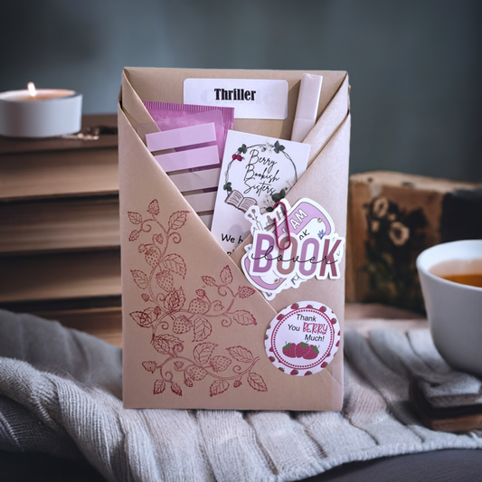 A packaged book subscription box labeled 'Berry Thrilling Book' with a floral design, placed on a cozy setting with a candle and a cup of tea in the background.
